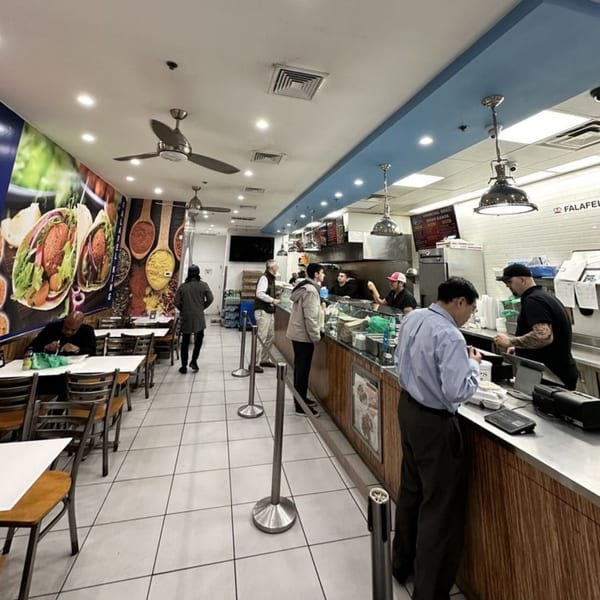 Customers ordering and dining inside Falafel King, a brightly lit Middle Eastern restaurant with large food murals.
