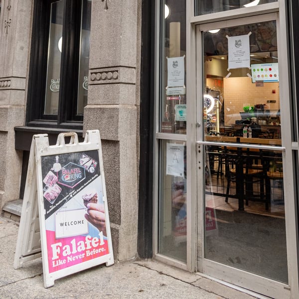 Falafel King storefront with a sandwich board sign and a view of the interior through the glass door.