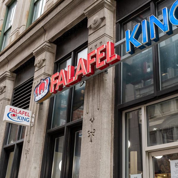 The Falafel King restaurant exterior with its red and blue neon sign on a stone building.