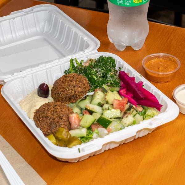 Falafel King takeout container with falafel, hummus, tabbouleh, cucumber salad, and pickled vegetables.