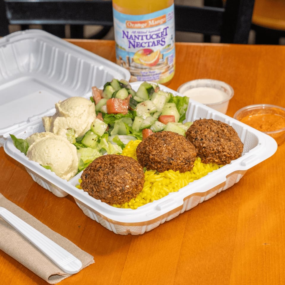 Falafel King's falafel plate with yellow rice, hummus, salad, and sauces, with a drink.