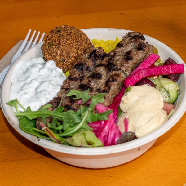 Falafel King's middle-eastern bowl with falafel, kebab, rice, hummus, tzatziki, pickled vegetables, and greens.