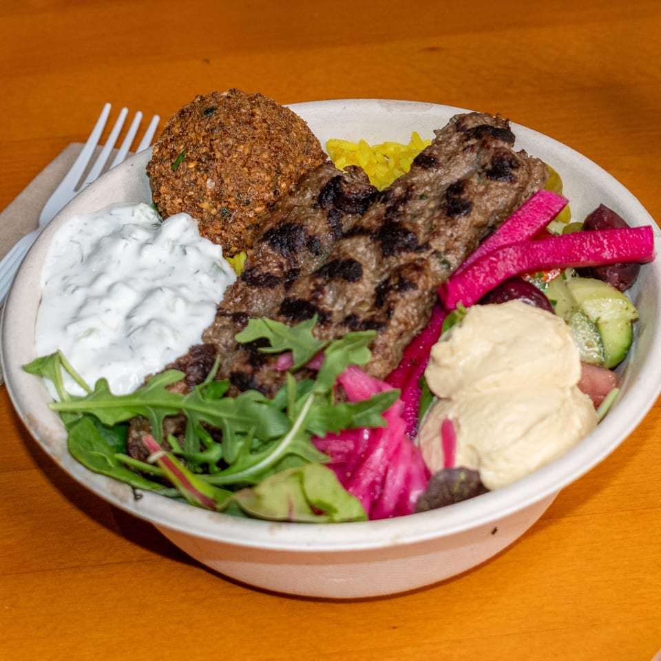 Falafel King's middle-eastern bowl with falafel, kebab, rice, hummus, tzatziki, pickled vegetables, and greens.