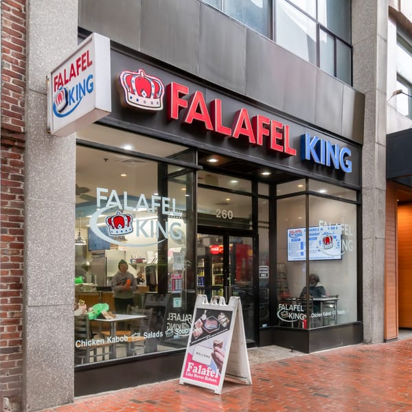 Exterior view of Falafel King restaurant with its prominent sign, glass storefront, and a sandwich board.