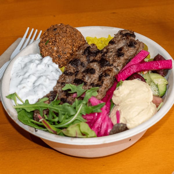 Falafel King's bowl with falafel, kebab, rice, hummus, tzatziki, pickled vegetables, and greens.
