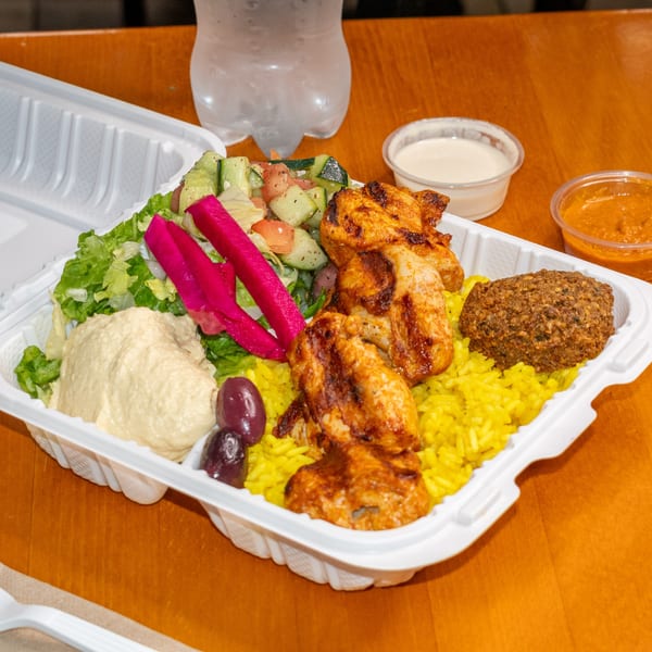 Falafel King's chicken and falafel platter with rice, hummus, salad, and pickled turnips in a to-go container.